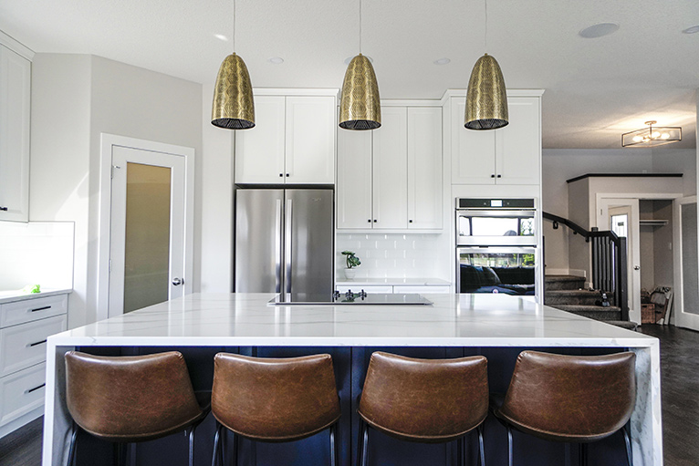 White kitchen with stool at a bar section and gold hanging lamps