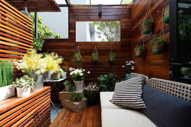 small outdoor space clad with wooden slatted walls and floor, decorated with lots of hanging plants and a seating area