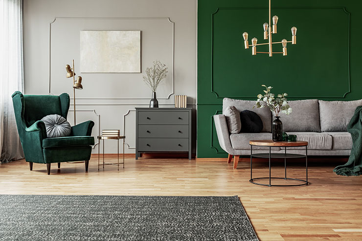 Photo of grey and green living room with green wing back chair, grey sofa and wooden commode.