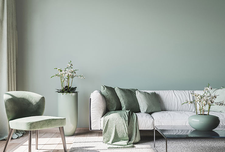 Photo of a pale green living room with grey sofa, pale green pillows, floor vase and plush chair.
