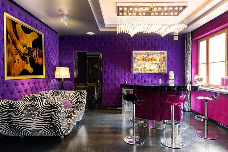 Violet and pink walls in a room with a tiger striped couch and a mini bar.