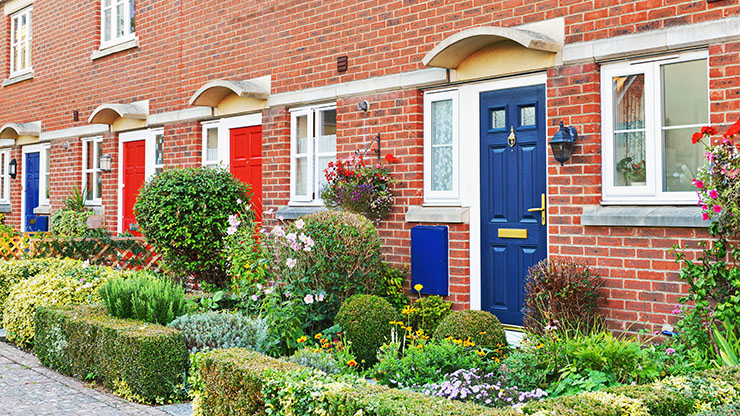 View of a home with a blue front door, red brickwork, and plants and flowers by the front door.