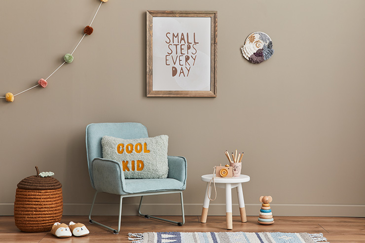 Cozy interior of child's room with mint armchair with a rectangular cushion saying 'Cool Kid' on it. The wall is painted beige with slogan wall art on the wall.