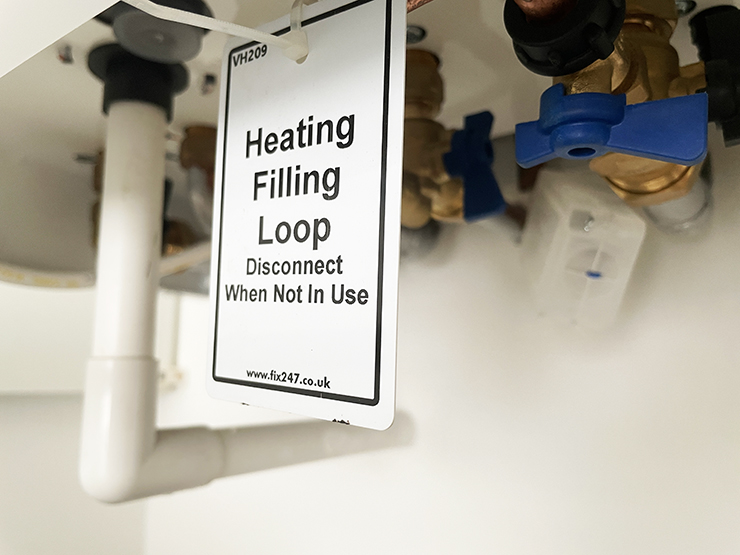 Picture of a sign hanging from a boiler which reads 'heating filling loop'