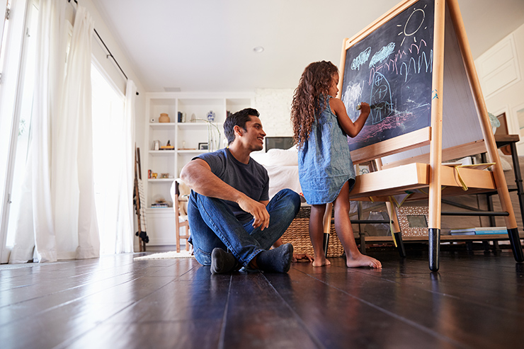 Picture of a father and daugther playing with a chalk board on wooden floors