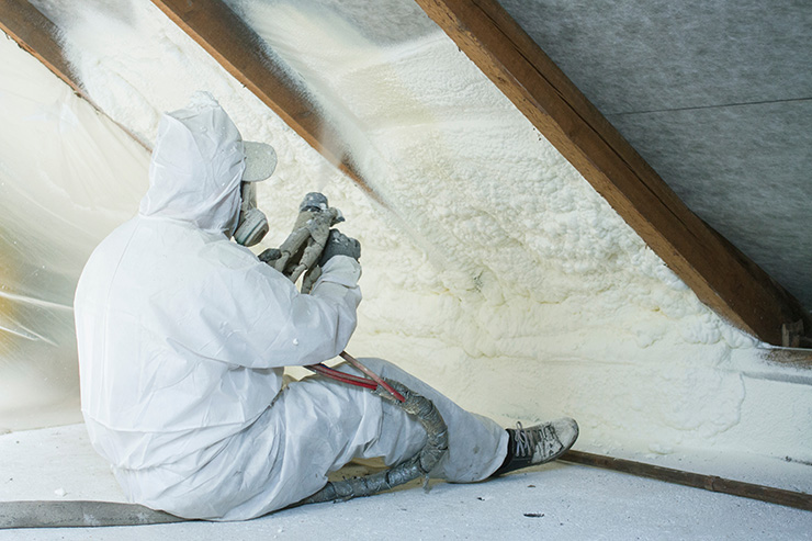 Picture of a seated tradesperson in a white protective suit and mask insulating a loft 