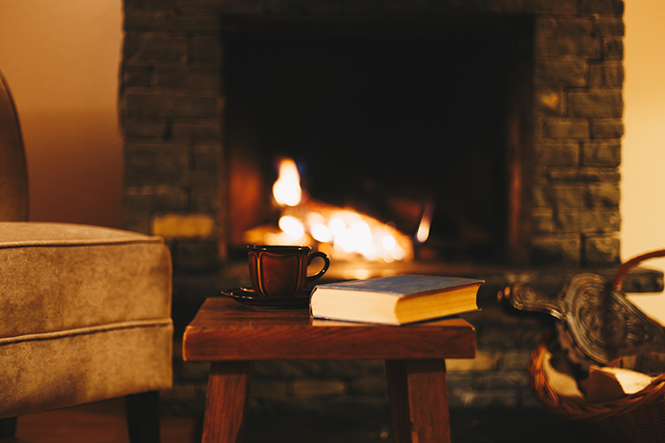 Picture of a coffee table with a book and mug and lit fireplace behind it