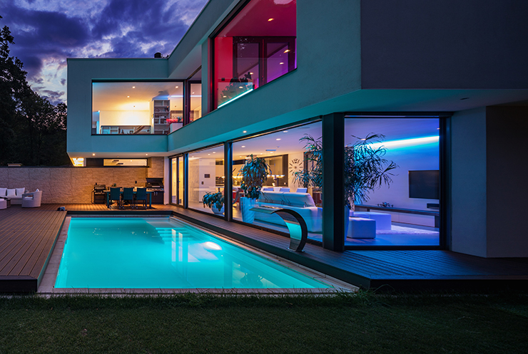 Picture of a swimming pool lit up at night next to luxury home