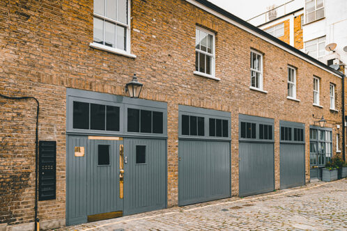 Picture of the front of a row of houses in a mews with grey garage doors and brick walls