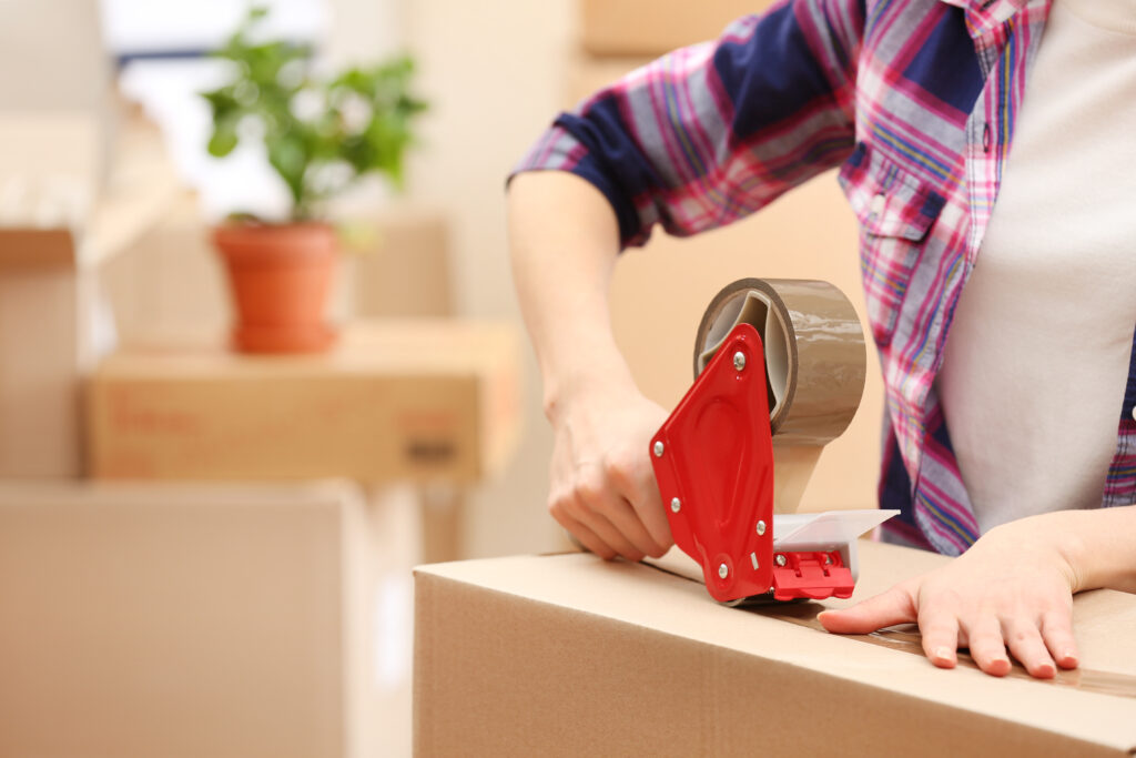 Picture of a hand holding tape dispenser taping a box shut