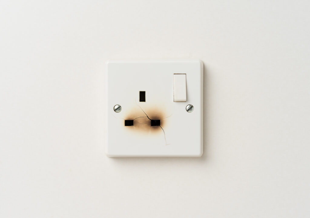 Picture of a plug socket on white wall with burnt scorch marks on it 