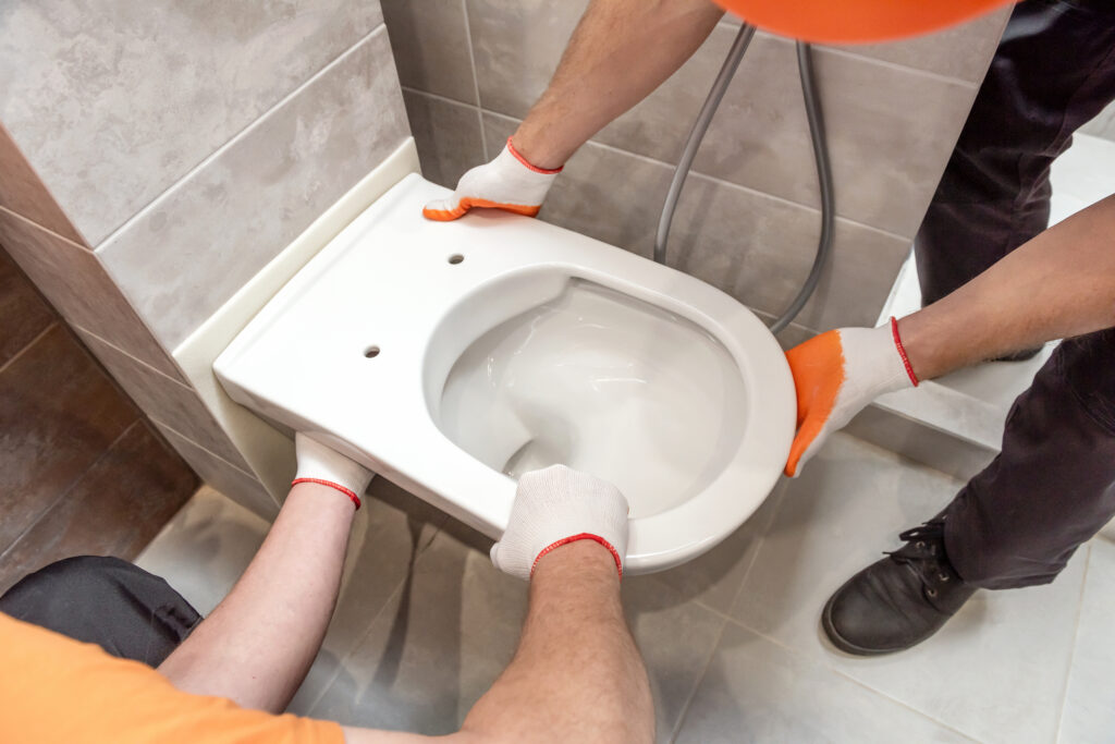 Oicture of two pairs of hands installing a wall-hung toilet to a bathroom wall