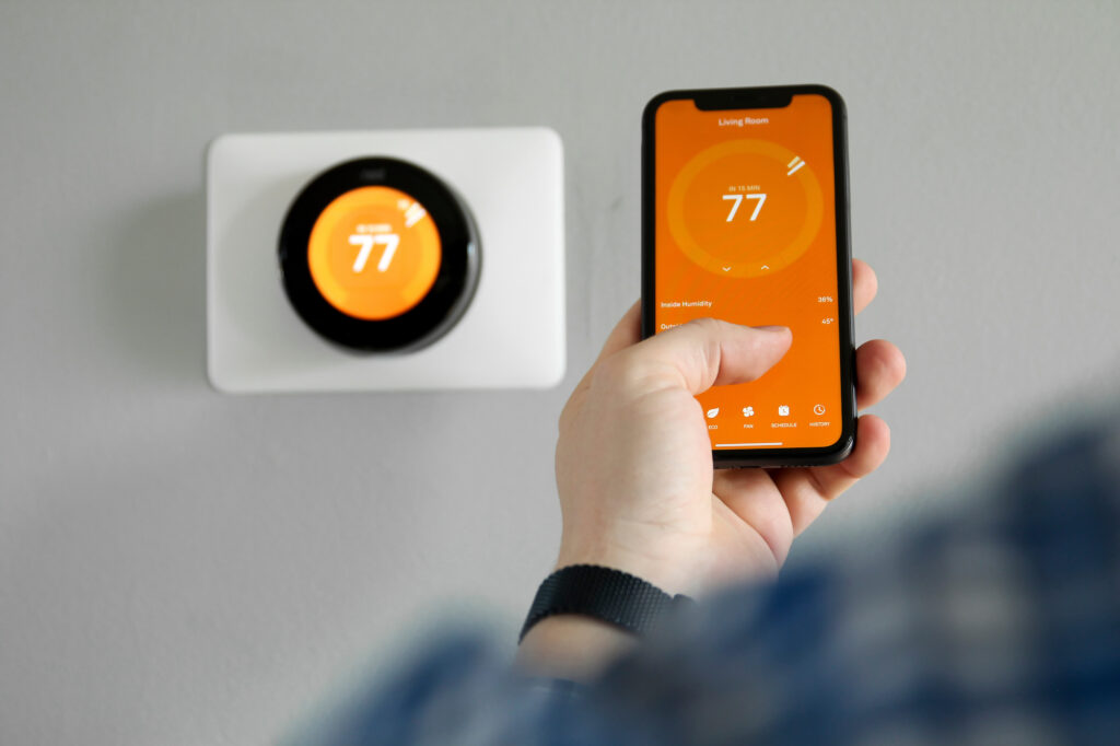 Picture of a man adjusting a smart thermostat using his phone 