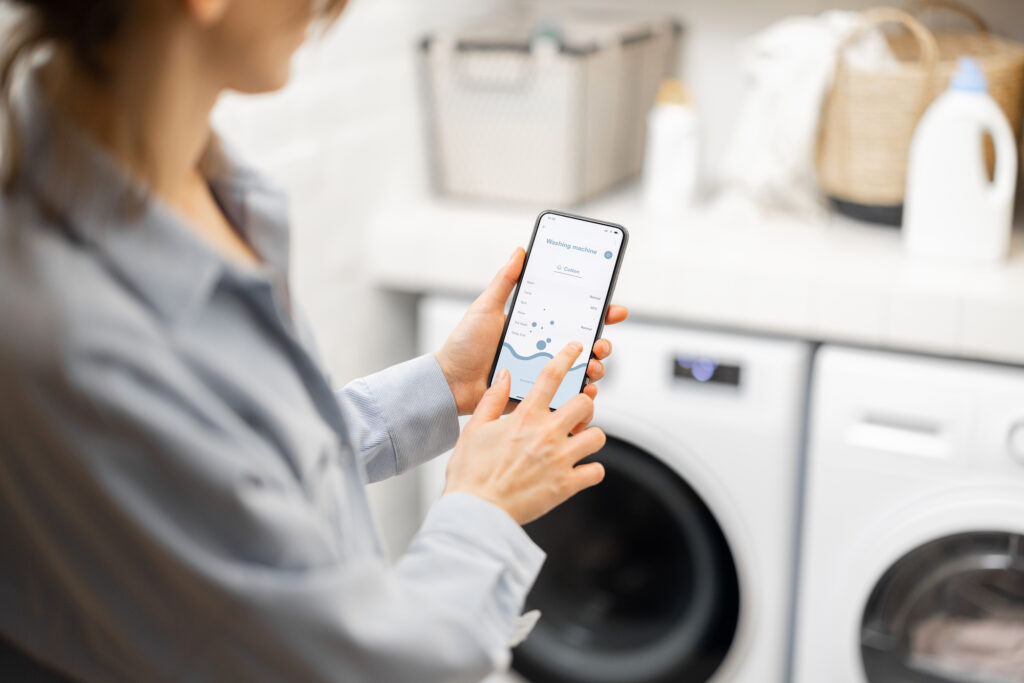 Picture of a woman using her phone to control her smart washing machine