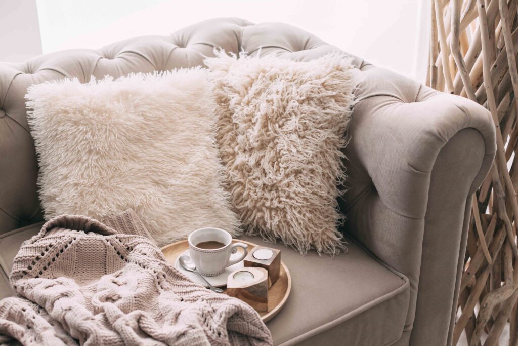 Picture of a sofa with cosy pillows and a cup of coffee on a wooden tray next to a blanket